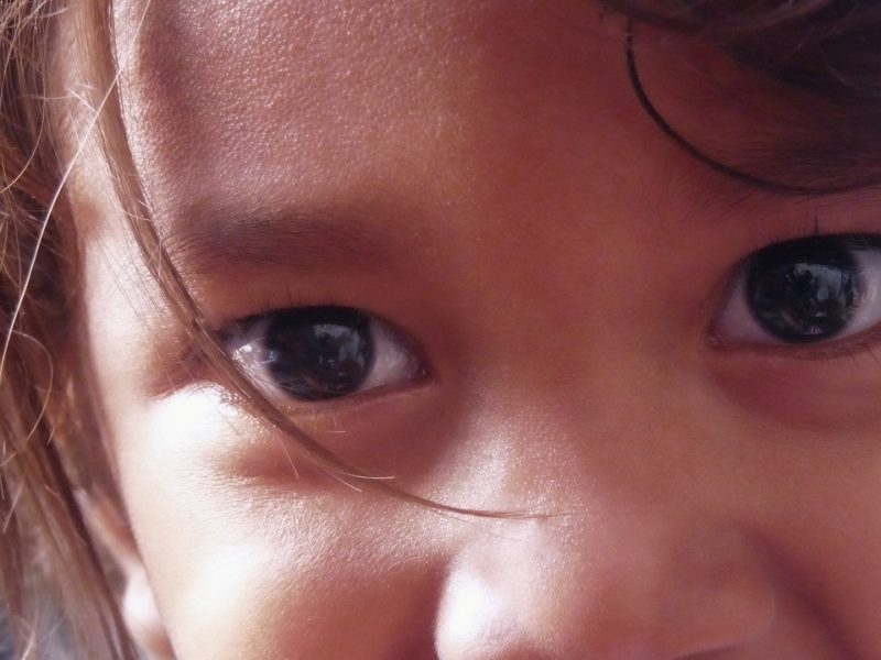 Close-up of a young child's face focusing on their eyes, with one eyebrow slightly raised. The child's gaze is expressive and curious, highlighted by soft, natural lighting.